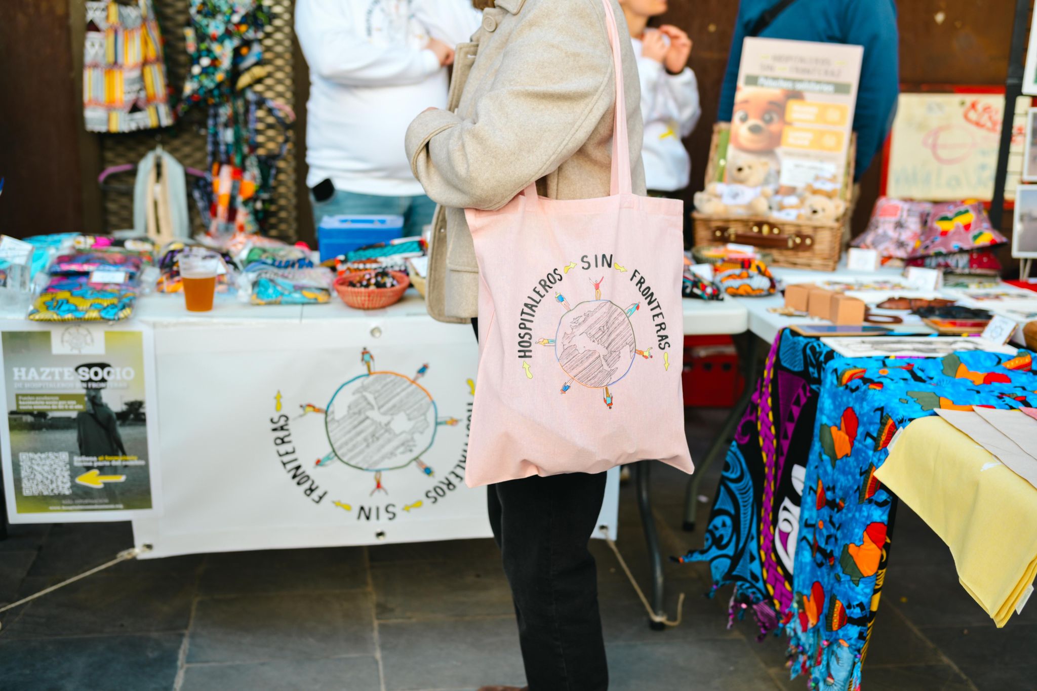 Productos de merchandising solidario de Hospitaleros Sin Fronteras expuestos durante una actividad benéfica.