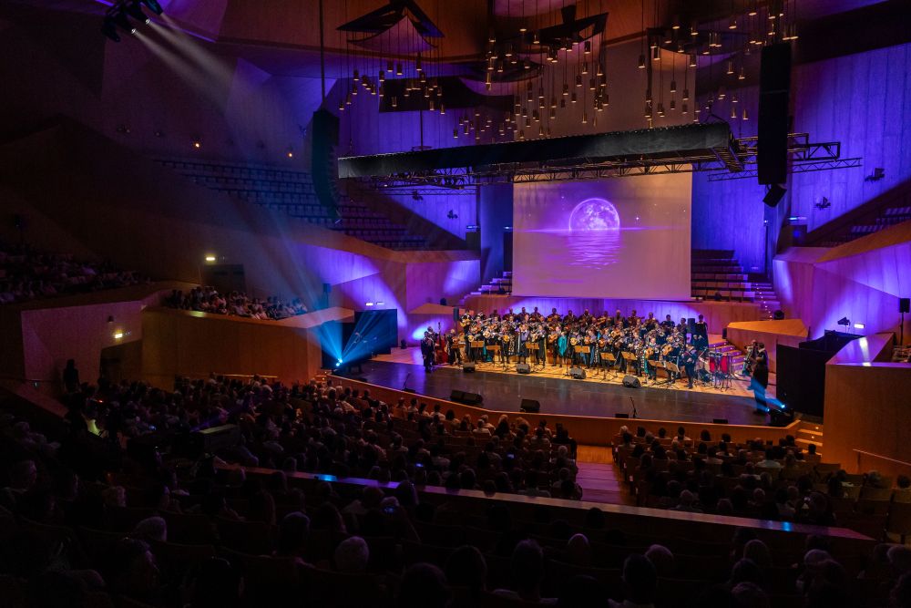 Vista panorámica del concierto solidario Voces que Importan en la Sala Mozart del Auditorio de Zaragoza con artistas sobre el escenario.